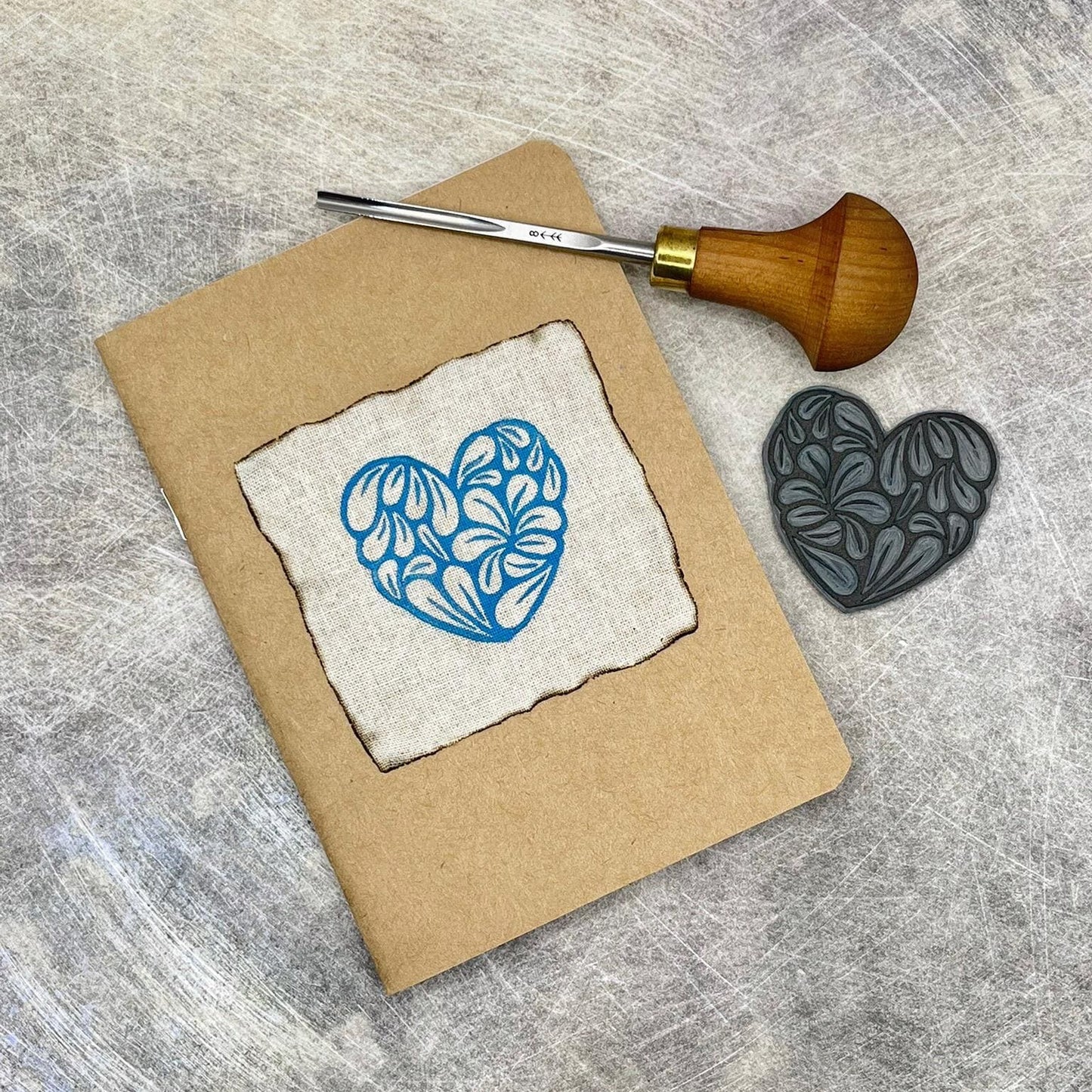 A6 Kraft notebook with original turquoise lino print on front. included in the photo is the lino and cutting tool used to make it.