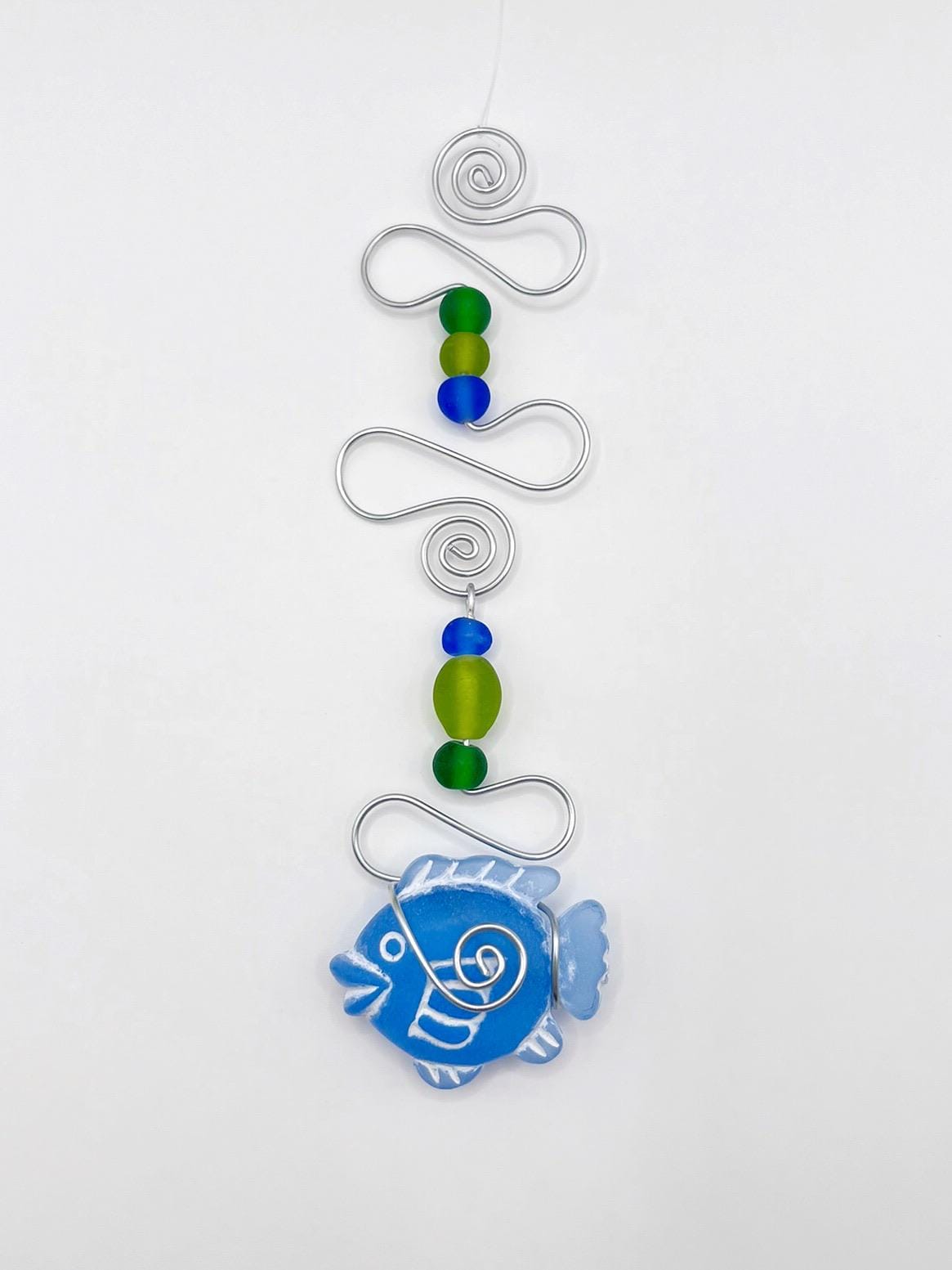 Decorative hanging with blue fish, wire and colourful beads on a white background