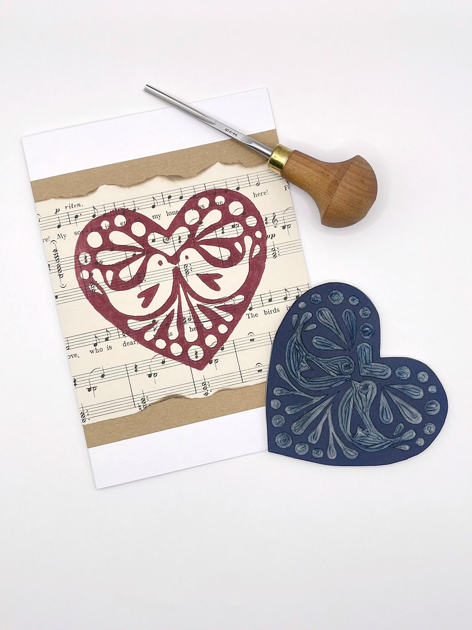 Card with heart design on sheet music. Photo includes lino and cutting tool used laid on a white background.