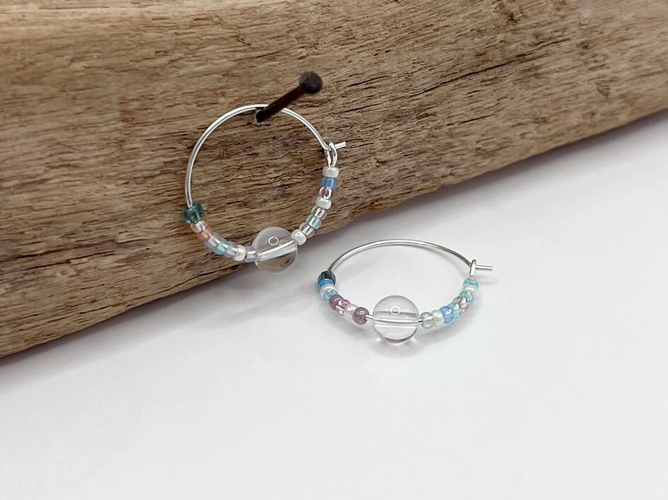 Pair of pastel seed bead and clear crystal hoop earrings hanging on driftwood against a white surface