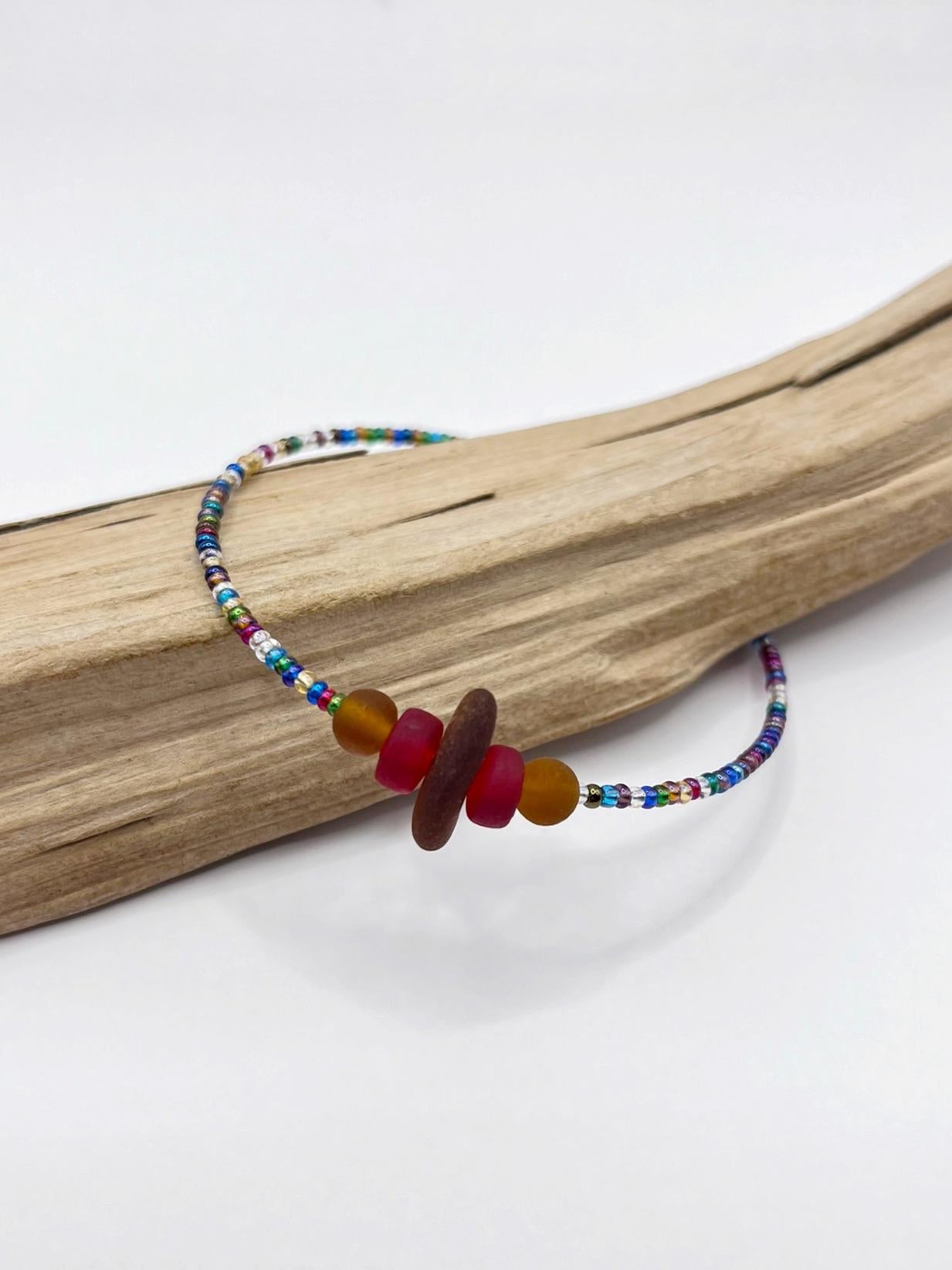 Rainbow beaded bracelet with sea glass and frosted glass beads on a piece of driftwood