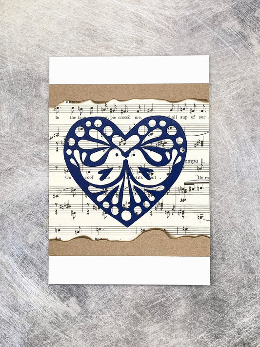 Card with blue original lino printed heart design on sheet music laid on a textured background.