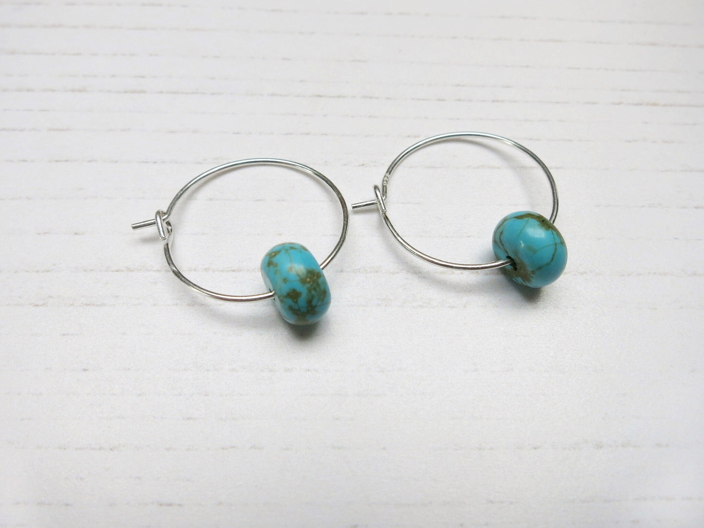 Close up of pair of hoop earrings with turquoise beads on a white background