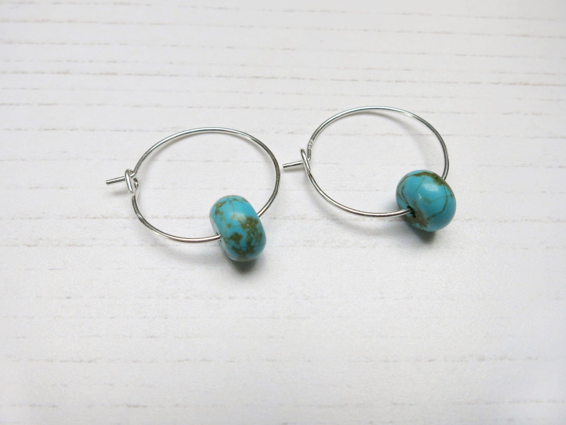 Close up of pair of hoop earrings with turquoise beads on a white background