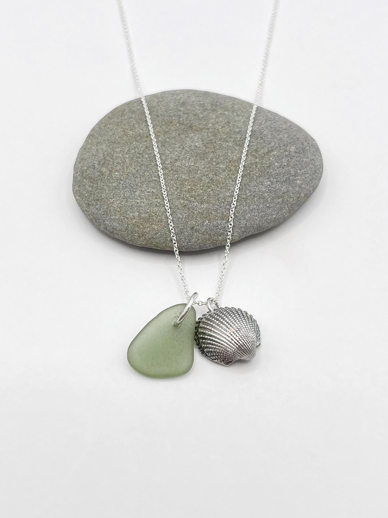 Necklace with green sea glass and a silver shell charm laid on a white surface