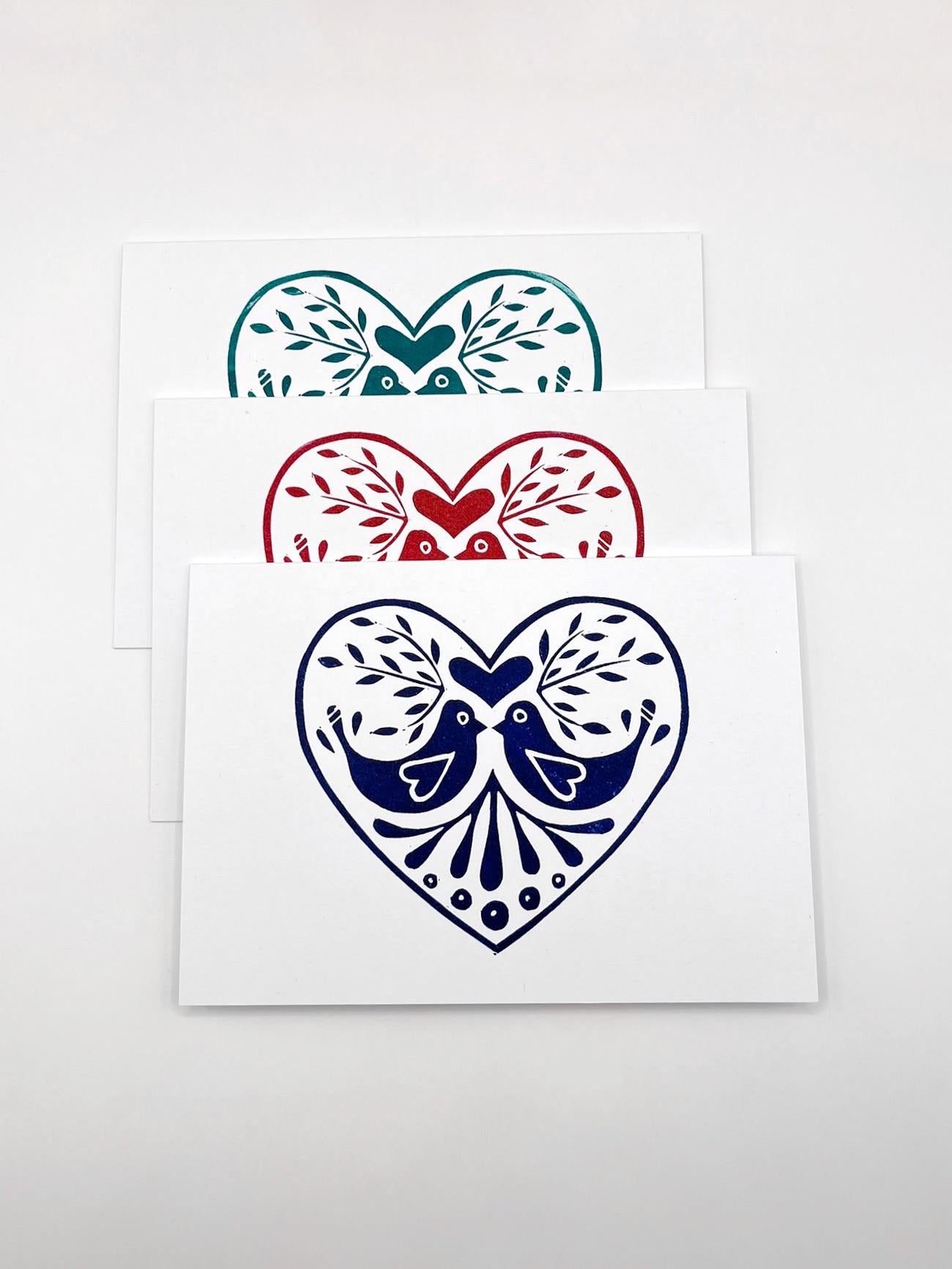Set of three original lino printed heart design cards in red, blue and green, laid on a white background.