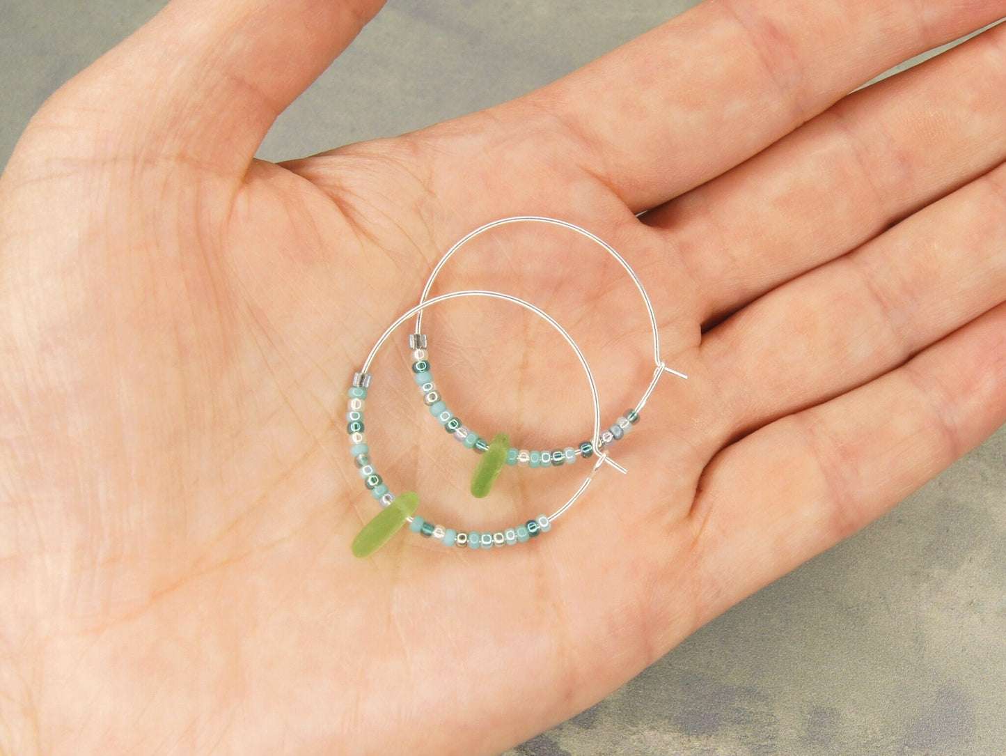 Turquoise seed bead hoop earrings with green sea glass laid on a hand