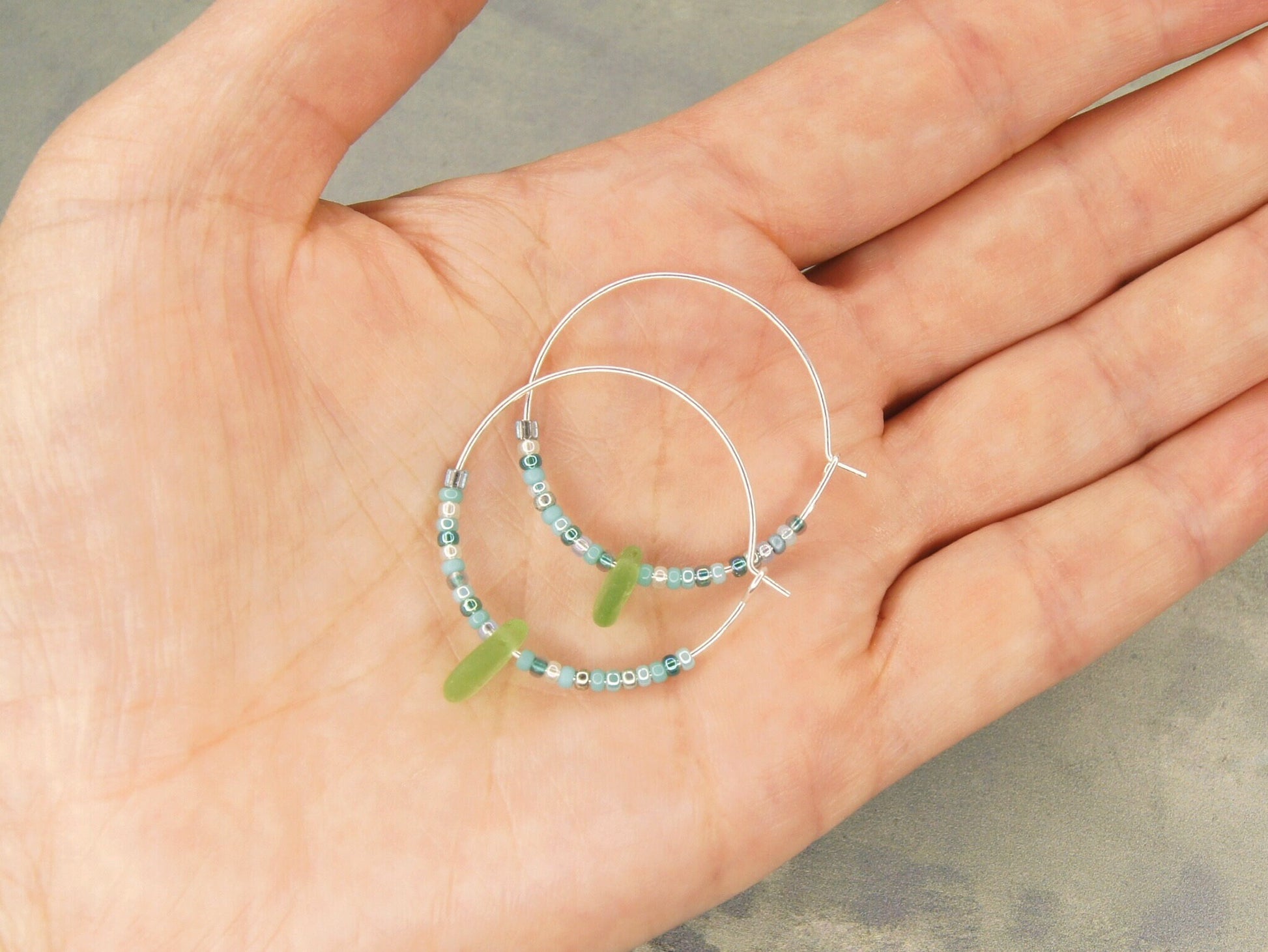 Turquoise seed bead hoop earrings with green sea glass laid on a hand