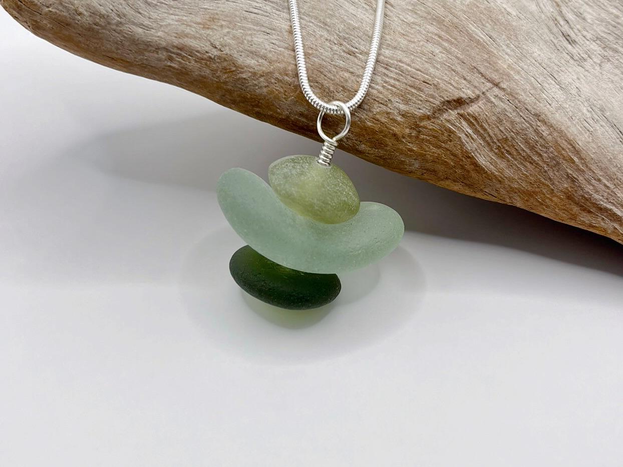Necklace with green sea glass and Jade pendant sat against driftwood on a white background