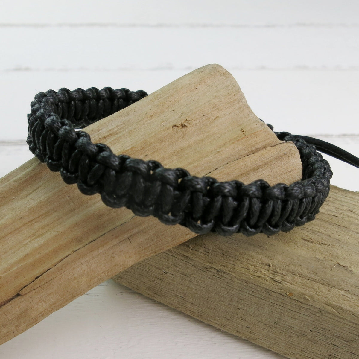 Black braided bracelet on a wooden block with a white background