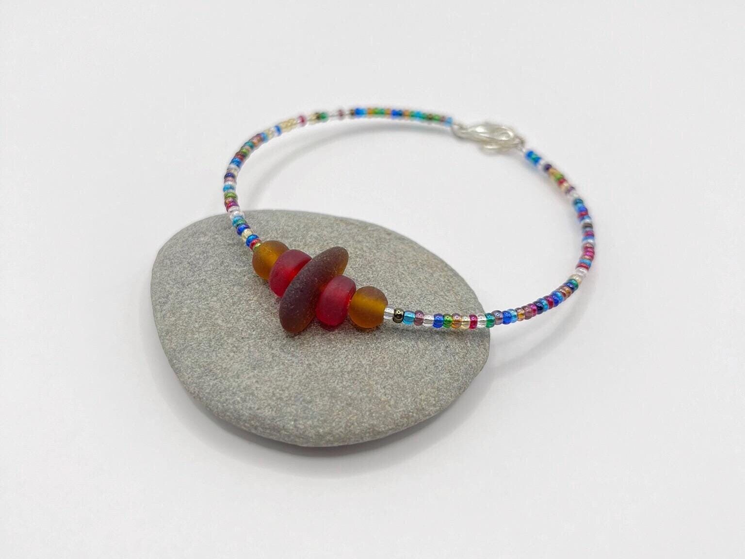 Colourful beaded bracelet with sea glass and red and brown beads laid on a grey pebble