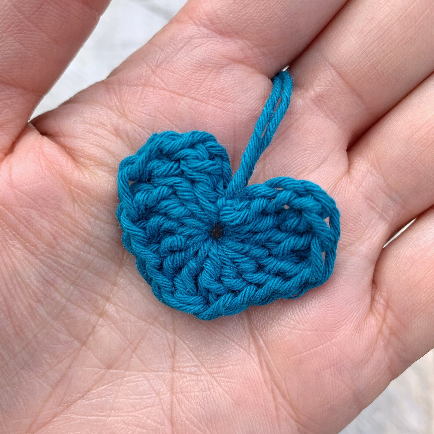 Teal crocheted heart held in a hand against a neutral background