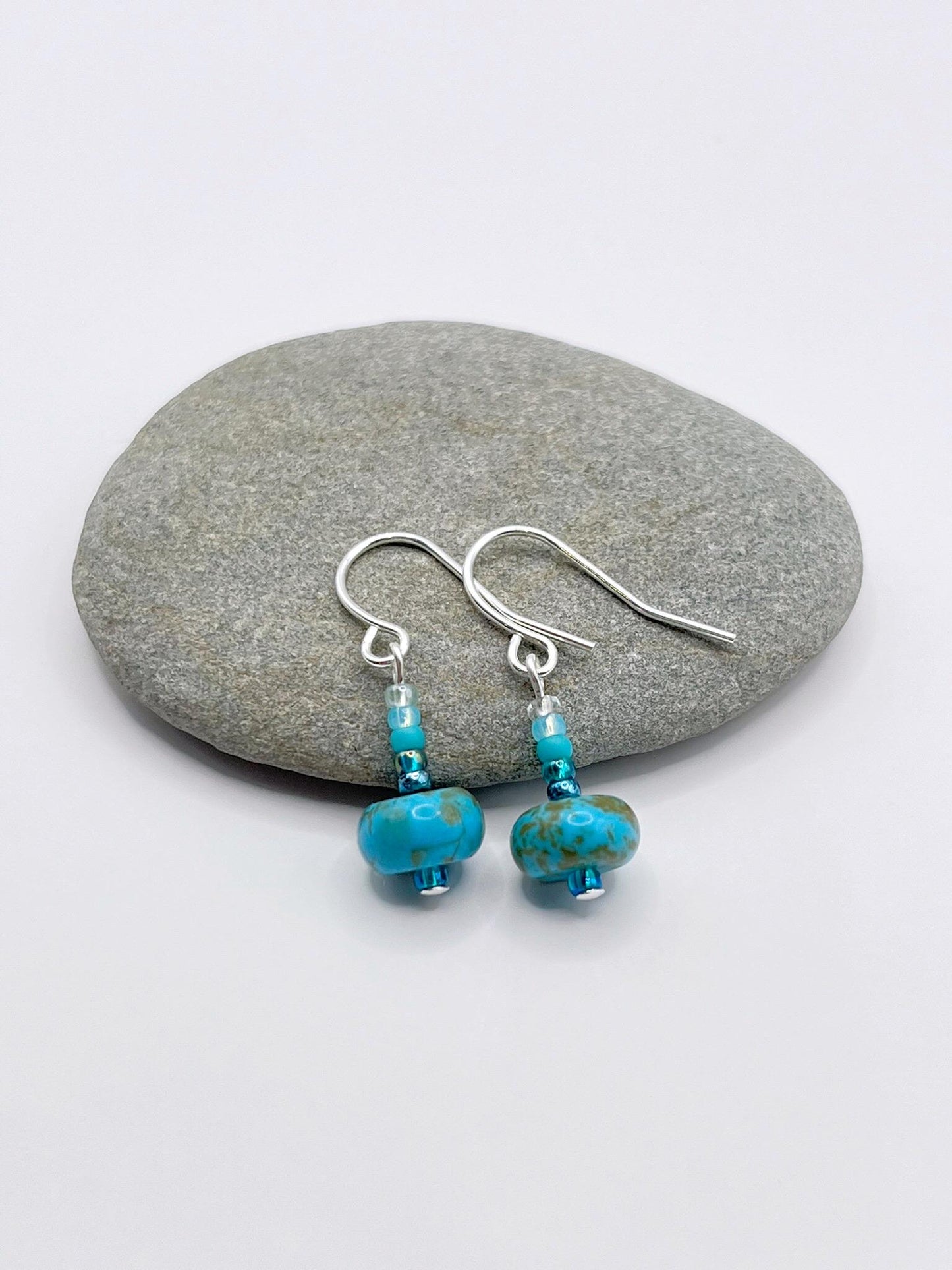 Turquoise beaded earrings laid on a grey pebble