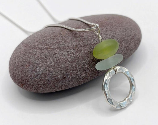 close up of sea glass and jade pendant with a hammered silver ring laid on a purple pebble
